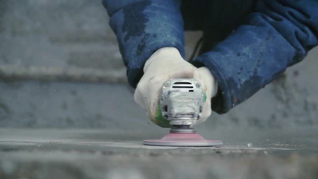 Builder worker with grinder machine cutting finishing concrete wall at construction site. Clip. Worker grinds concrete wall