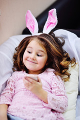 baby girl with rabbit ears with mobile phone or with smartphone in hands lies on sofa and smiles.