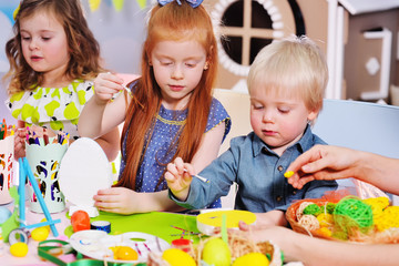 children in kindergarten paint eggs for the Easter basket at the table.