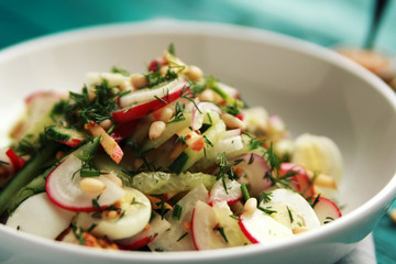 Salad with vegetables and eggs on the colorful blue background. Close up. European cuisine. Radish, cucumber, quail eggs and pine nuts. Ovo vegetarian dish.
