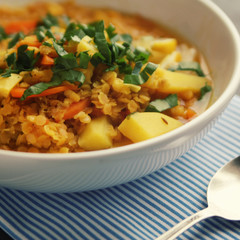 Red lentil stew on the round white plate. Close up. Vegan dish with potato, carrot and turmeric. European cuisine. Vegetarian lunch. Toned photo.
