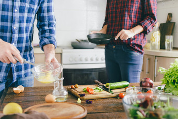 Couple cooking together healthy breakfast of vegetables and scrambled eggs on wooden table in home kitchen