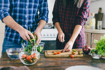 Couple cooking together summer salad of vegetables on wooden table in home kitchen