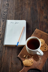 Cup of tea with cookies, workbook and a pencil on a wooden background, top view