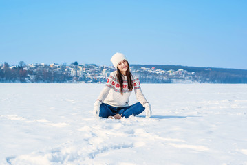 Girl in a white winter sweater Sits with crossed legs in the snow. Throws the snow up.