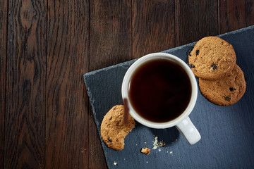 Cup of tea with cookies on a cutting board on a wooden background, top view