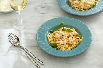 Plate of spaghetti carbonara with glass of white wine on white wooden table. Dinner table concept