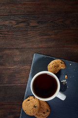 Cup of tea with cookies on a cutting board on a wooden background, top view
