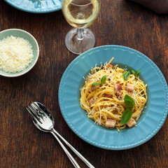 Plate of fresh homemade pasta carbonara with a glass of white wine on a wooden table, top view