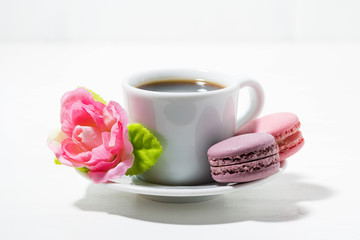 macaroon cookies, cup of coffee and flowers on white table