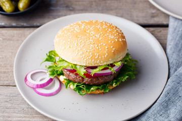Burger on a plate with pickles. Wooden background.