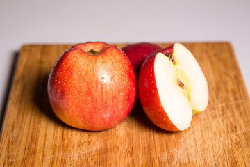 Three red apples with shadow on a wooden board