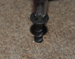 Black screw wrapped in a sheet of chipboard with a screwdriver or a drill.