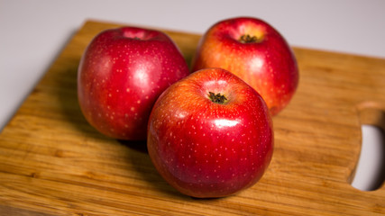 Three red apples with shadow on a wooden board