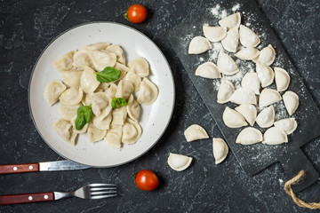 Traditional russian pelmeni, ravioli, dumplings with meat on black concrete background. Top view