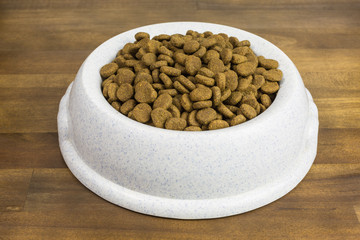 plastic bowl of dog food pellets on wooden background