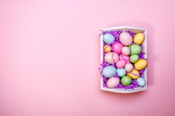 Multicolor eggs in a white tray. Creative Easter concept. Modern solid pink background.