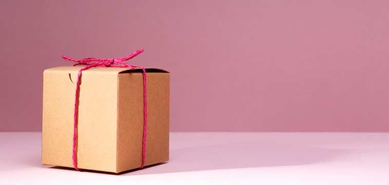 Craft cardboard gift box on the solid pink background. Holiday and gift concept