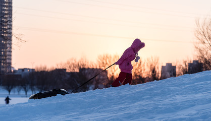 A child is pulling tubing on a snowy mountain at sunset