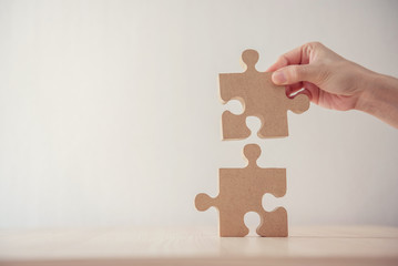 Closeup hand of woman connecting jigsaw puzzle on table wood, Business solutions, success and strategy concept