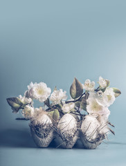 Easter concept with eggs and decorative white blossom bunch on pastel blue background, front view, copy space