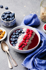 Smoothie bowl with fresh raspberry, blueberry, coconut flakes and chia seeds. Grey stone background.
