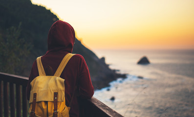 Fototapeta premium Hipster hiker tourist with backpack looking of amazing seascape sunset on background sea, girl enjoying ocean horizon, panoramic sunrise, traveler relax holiday concept, sunlight view in trip vacation