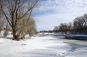 Springtime.Sunny landscape with  trees growing on the bank of river.Melting snow and ice.White clouds in spring blue sky.River Upa in Tula region,Russia. 