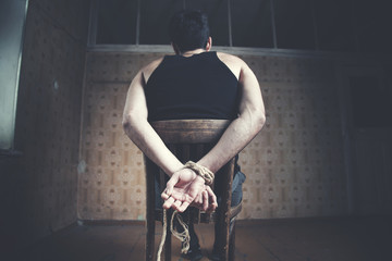young man tied to chair on dark background