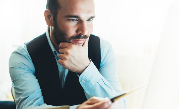 Bearded young businessman working on modern office at night. Consultant man thinking looking in monitor computer. Manager typing on keyboard in coworking workplace, startup project concept in studio