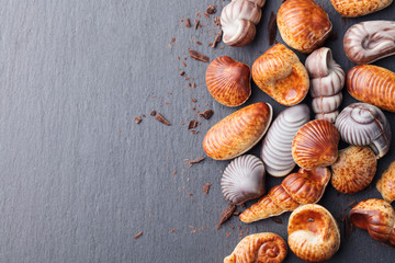 Chocolate candies, traditional Belgian shell shape. Black slate background. Top view. Copy space.