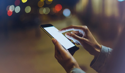 hipster using in hands clean gadget mobile phone closeup, blogger pointing finger on blank screen smartphone on background bokeh light in night atmospheric city, online wifi internet concept