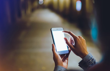 Woman pointing finger on blank screen smartphone on background bokeh light in night city, hipster blogger using in hands clean gadget mobile phone, mockup street, online wifi internet concept