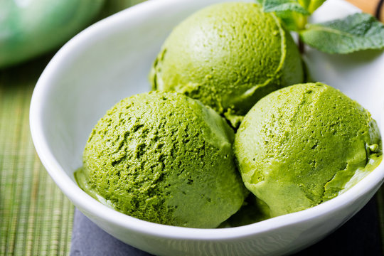 Green tea matcha ice cream scoop in white bowl on a wooden background. Close up.