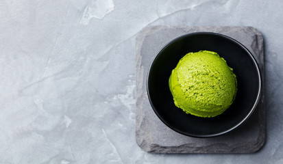 Green tea matcha ice cream scoop in black bowl on a grey stone background. Copy space. Top view.