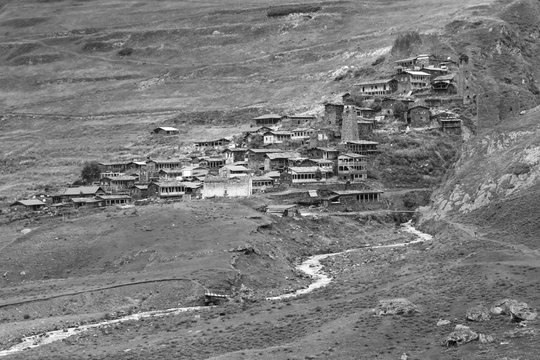 Remote medieval Tushetian village with defencive towers (Dartlo, Georgia). Hills covered with grass. Some huge stones could be seen on the foreground. The river runs down the hill. Black and white.