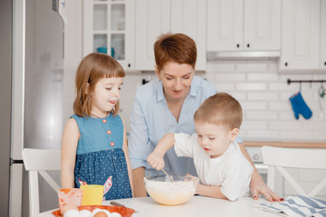 Family cooking. Mom with children boy and girl preparing dough for cupcakes, boy interferes with...