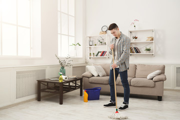 Young man cleaning home with mop