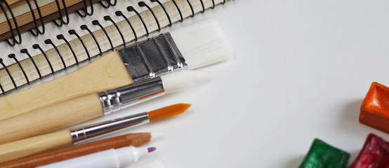 Watercolor paints and notepad on white wooden desk, top view, copy space