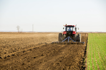 Fototapeta premium Farmer in tractor preparing land with seedbed cultivator as part of pre seeding activities in early spring season of agricultural works at farmlands.
