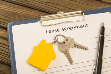 lease contract, pen, keys with a key ring in the form of a house on a wood background. rental of property.