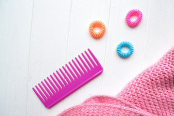 Pink comb and bright spiral scrunchies on the white wooden desk. Bright beauty background with place for text.