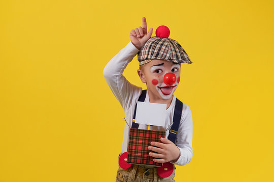 Cute little boy clown in a costume, makeup.Funny kid clown fooling.Young child shows expression face joy,smile,cheerful.1 April fool's day celebration.Concept holiday, birthday,laughter,jokes,party.