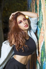 Fototapeta premium beautiful redhead hispanic girl posing by a wall with colorful graffiti, urban style with casual and modern clothes