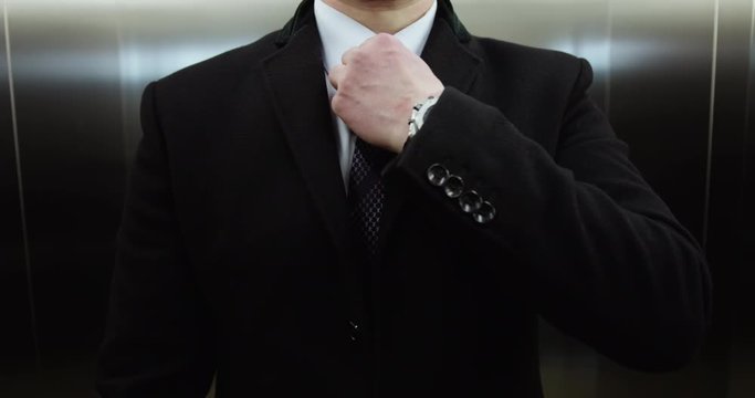 Man straightens his tie in elevator