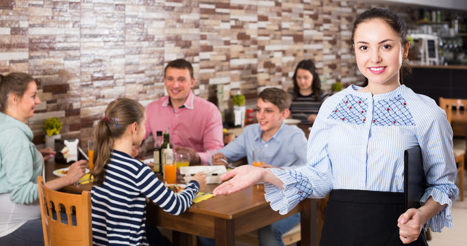 Positive waitress holding tray with dishes meeting visitors