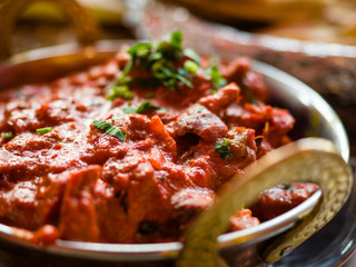 Indian Food or Indian Curry in a copper brass serving oriental bowl, pieces of chicken fillet in curry sauce ingredients in a pan with the old table side view close-up, Set of Indian food.