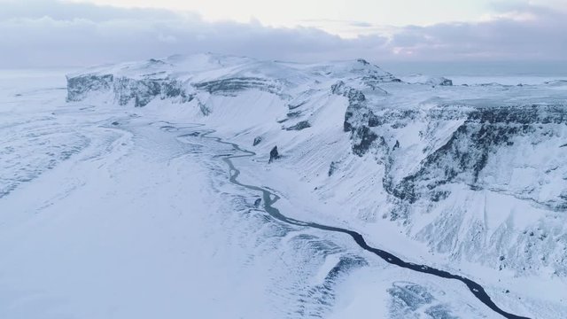 Aerial shot turning and revolving around a mountain in winter landscape. Snow covered land and creek; white winter.