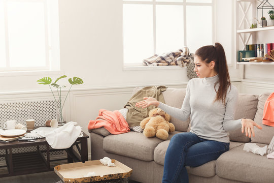 Desperate woman sitting on sofa in messy room