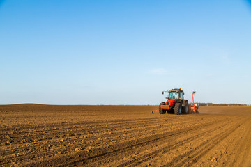 Fototapeta premium Farmer seeding, sowing crops at field. Sowing is the process of planting seeds in the ground as part of the early spring time agricultural activities.